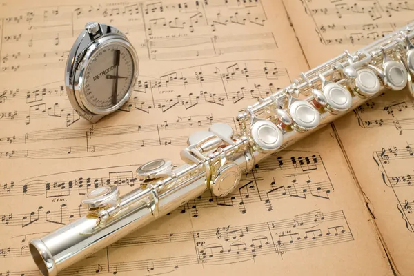 Stříbrná flétna a pocket metronom na staré hudby skóre — Stock fotografie
