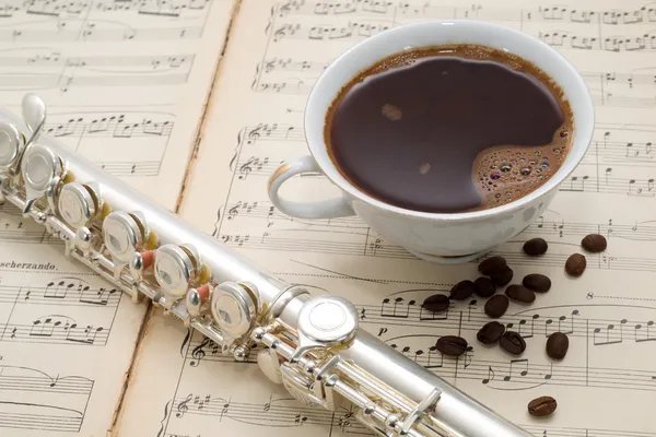 Flauta de prata, xícara de café e grãos de café em uma partitura de música antiga — Fotografia de Stock