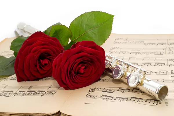 Flute and beautiful red rose on an ancient music score — Stock Photo, Image