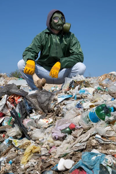 Man in a gas mask sitting on the garbage and holding a bone — Stock Photo, Image