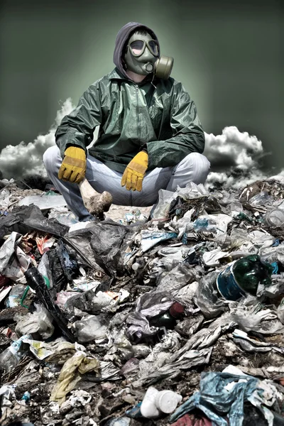 Man in a gas mask sitting on the garbage and holding a bone — Stock Photo, Image