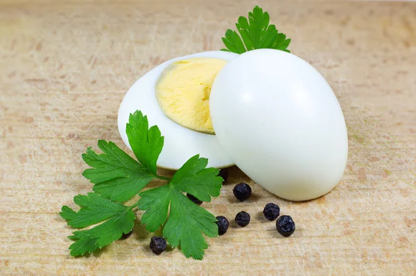 Deux demi d'oeuf cuit avec du persil et du poivre sur une planche de bois — Photo