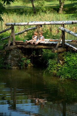 Adorable Little Twin Brothers Sitting on the Edge of Wooden Bridge and Fishing on Beautiful Lake clipart