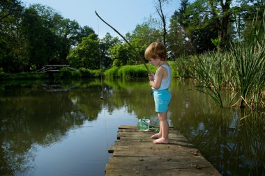 Adorable Little Boy Fishing from Wooden Dock on a Lake in Sunny Day clipart