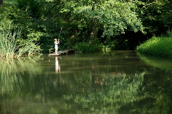 Malý chlapec rybaření od okraje dřevěná dok na jezero obklopené krásnou přírodou — Stock fotografie