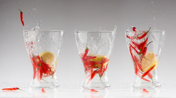 Πιτσιλίσματα νερού από το κόκκινο καυτό πιπέρι και λεμόνι σε ένα ποτήρι. κολάζ. οξεία φρεσκάδα έννοια — Φωτογραφία Αρχείου
