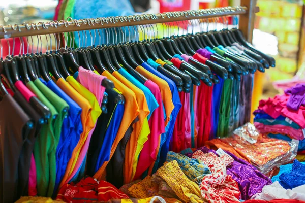 Um rack de camisas coloridas penduradas para venda em uma feira — Fotografia de Stock