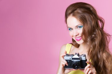 bir kamera tutarak pembe bir arka plan üzerinde genç güzel kadın