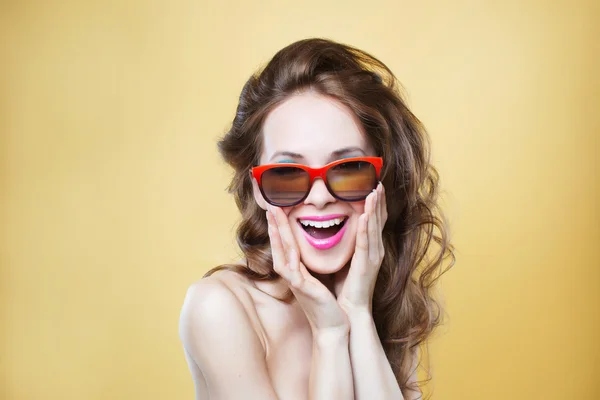 Attractive surprised young woman wearing sunglasses on gold back — Stock Photo, Image