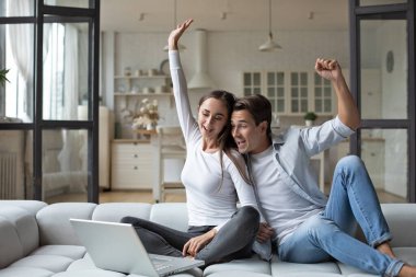 Happy couple winners screaming with joy sitting on the couch at home. 