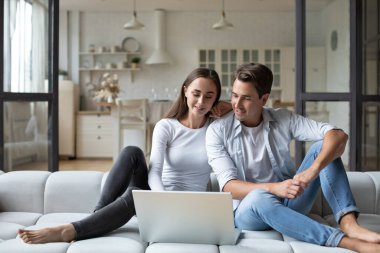 Smiling young couple relaxing on a couch at home, using laptop computer.