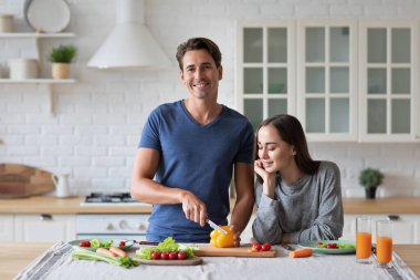 Beautiful young couple cooking vegetable salad while standing in the kitchen at home, enjoying time together. Healthy lifestyle concept.