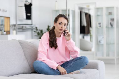 Serious woman talking on mobile on the couch at home.