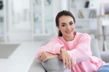 Kanepede oturmuş gülümseyen güzel, sakin, mutlu bir kadının portresi. Pembe bir kazakla içeride poz veren kız öğrenci..