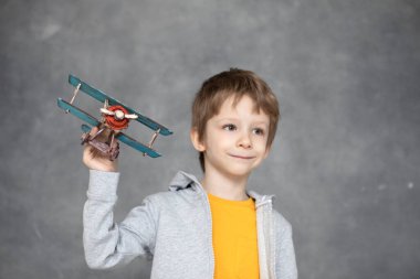 Evdeki gri duvarın üzerinde uçan tahta uçak oyuncağıyla oynayan sevimli çocuk. Mutluluk ve özgürlük kavramı.