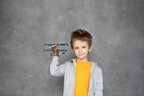 自宅の灰色の壁を飛んで木製の飛行機のおもちゃで遊んでかわいい男の子 幸福と自由の概念 — ストック写真