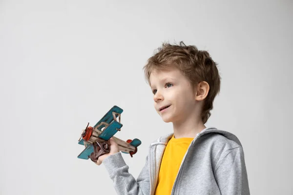 白い背景の上で 彼の手の中に木製の飛行機でかわいい男の子を笑っている 幸福と自由の概念 — ストック写真