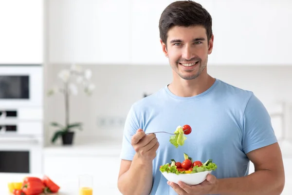 キッチンで喜んでUnshaven笑みを浮かべて男は彼の手の中に野菜サラダとプレートを保持し 良い青いTシャツを着ているようだ 健康的でベジタリアンフードのコンセプト — ストック写真