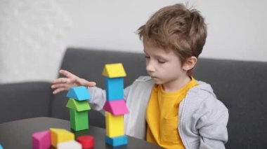 Küçük çocuk oturma odasındaki renkli ahşap bloklardan ev inşa ediyor. Yavaş çekim görüntüleri.