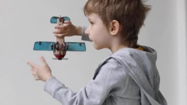 Beyaz arka planda tahta bir oyuncak uçakla oynayan şirin bir çocuk. Çocuk evde eğleniyor..