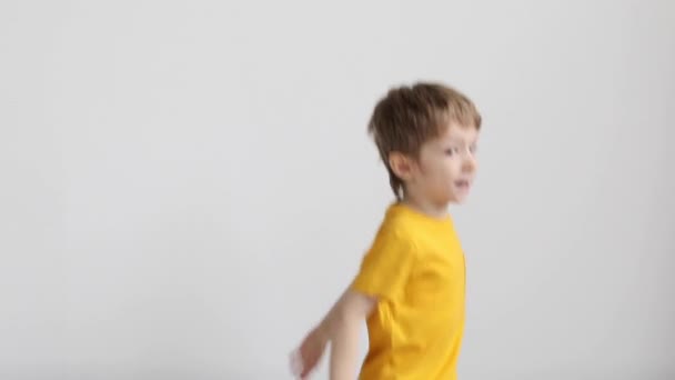 穿着黄色T恤的快乐孩子在家里的沙发上跳着 背景是白色的 — 图库视频影像