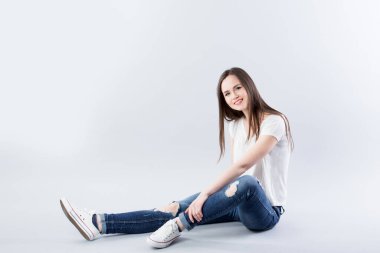 Beyaz tişörtlü ve kot pantolonlu güzel bir kadın stüdyoda yerde tek başına oturuyor..