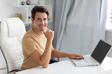 Masada dizüstü bilgisayarı olan gülümseyen genç adam. Bağımsız, uzaktan kumandalı bir salgın..