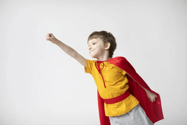赤いマントの小さなスーパーヒーローの笑顔は 白い背景で飛行を示しています パワーコンセプト 家で遊んでる男の子 — ストック写真