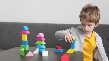 Evde ahşap bloklar inşa eden küçük bir çocuk, gelişim faaliyetlerinden zevk alıyor. Yavaş çekim görüntüleri.