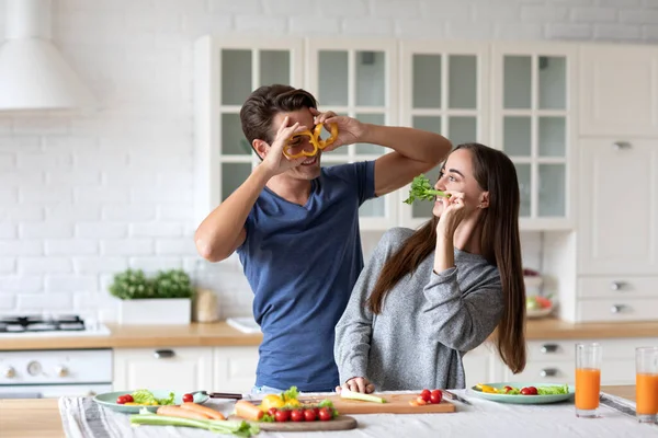 家庭でキッチンで料理をしながら楽しい時間を過ごすことを愛する正の若いカップル ピーマンスライスから眼鏡を作る 一緒に健康的な料理を楽しむ — ストック写真