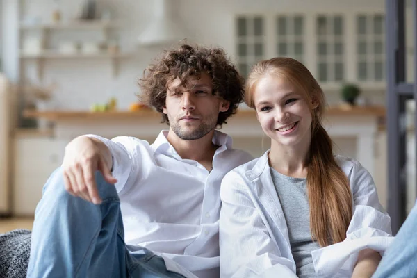 Kanepede oturan genç çift kameraya bakıyor. Evde birlikte iyi eğlenceler..