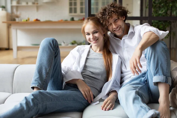 Kanepede oturan genç çift kameraya bakıyor. Evde birlikte iyi eğlenceler..