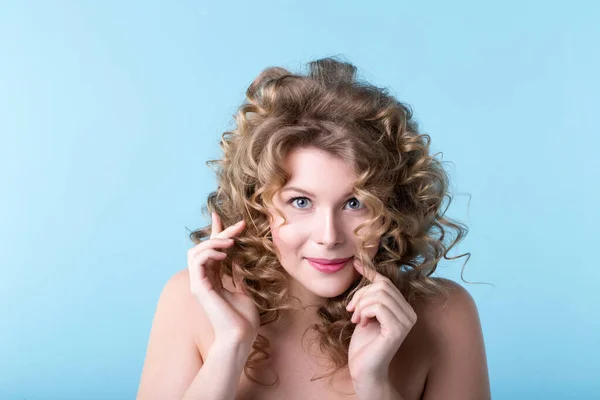 青い背景に巻き毛の笑顔の若い美しい女性 スタジオの女性の感情的な肖像画 ストック写真