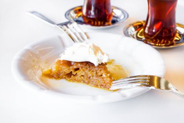 Geleneksel Türk Ekmek Pastası Tatlısı pıhtılaşmış kremayla, çatal ve çayla beyaz üzerine.