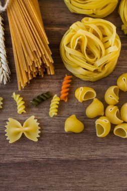 Ahşap masadaki çeşitli pişmemiş makarna ve makarnaların fotokopi alanı ve dikey görüntüsü var.