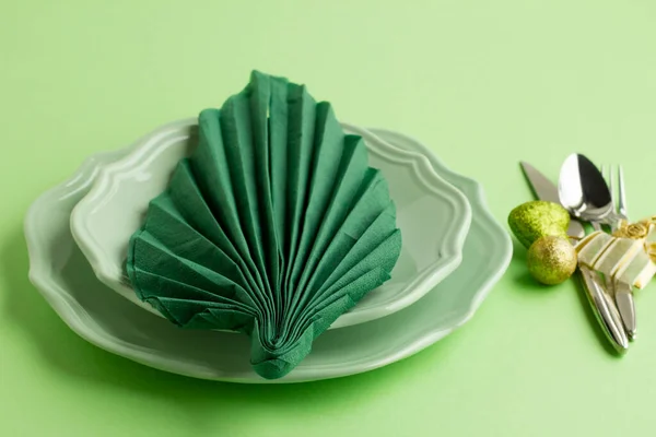 Green leaf-shaped folded christmas napkin on the plate with cutlery set