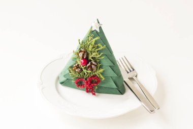 Katlanmış yeşil noel ağacı kağıt peçetesi beyaz tabakta çatal bıçak takımı ve kopyalama alanı.