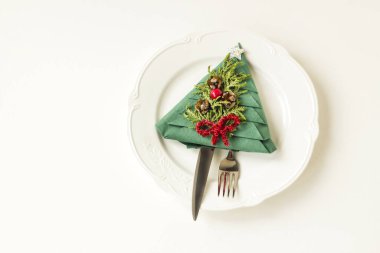 Katlanmış yeşil noel ağacı kağıt peçetesi beyaz tabakta çatal bıçak takımı ve kopyalama alanı.