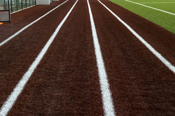 Empty,running track with white lines in stadium next to green ground