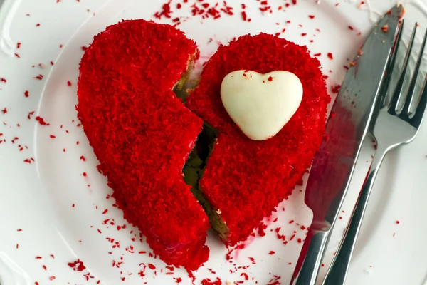 Sweet,red,wet cake cut in half like broken heart in the white plate with knife and fork.Valentine\'s Day concept.