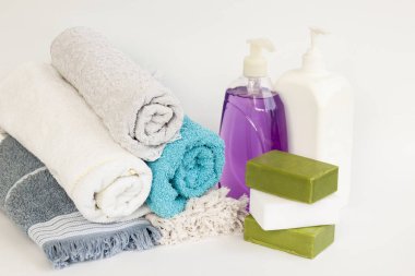 Yuvarlanmış çok renkli banyo ve beyaz arka planda yüz havluları doğal zeytinyağı sabunları ve sıvı sabunlarla.
