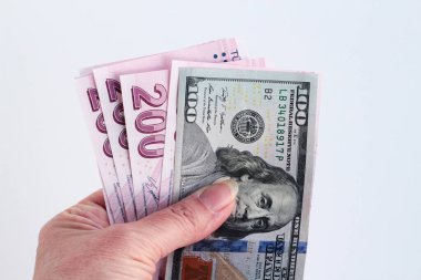 Beyaz zemin üzerinde 100 Amerikan doları ve Türkçe 200 banknot tutuyor.