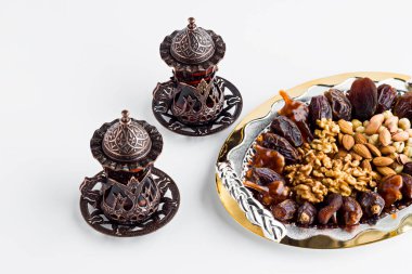 Lüks kurutulmuş tarih meyveleri, ceviz, şam fıstığı, fındık ve bademle altın tepside dizayn edilmiş, beyaz yüzeyde çay ile birlikte. Ramazan ayının kavramsal görüntüsü..