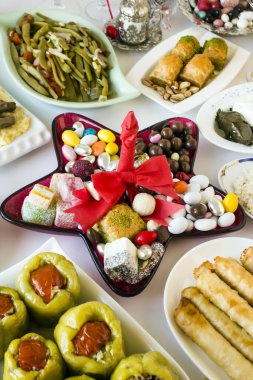 Ziyafet için sofra hazırlayan Bayram sofrasi, masanın ortasına yıldız şeklinde kırmızı şeker tabağı dizayn edilmiş geleneksel Türk gıdalarıyla.