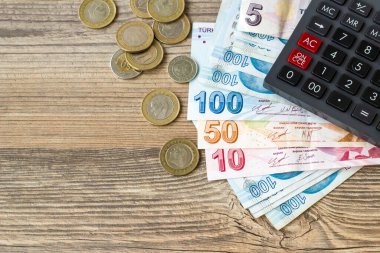 Tahta yüzeyde Türk Lira Banknotları, madeni paralar ve bir hesap makinesi var.