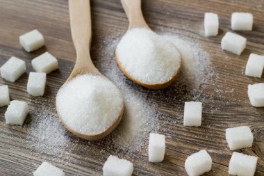 Tahta kaşıklarda granüle şeker ve tahta yüzeyde küp şeker.