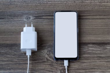 Beyaz beyaz ekranlı akıllı telefon ahşap yüzey ve şarj aleti