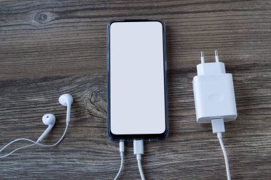 Şarj aleti ve kulaklığı olan ahşap yüzeyde beyaz beyaz ekranlı akıllı telefon.