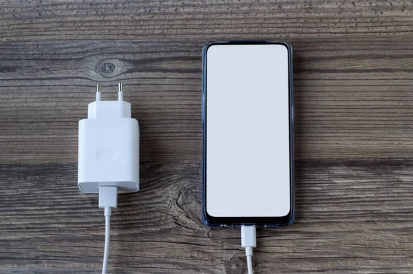 Beyaz beyaz ekranlı akıllı telefon ahşap yüzey ve şarj aleti