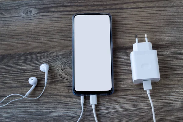 Şarj aleti ve kulaklığı olan ahşap yüzeyde beyaz beyaz ekranlı akıllı telefon.